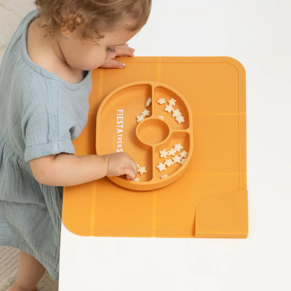 Child playing with a yellow plate and placemat on a white background