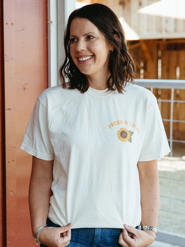 Woman wearing a white t-shirt with a sunflower design and text, standing outdoors.