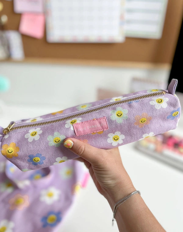 Hand holding a purple pencil case with floral patterns on a blurred background