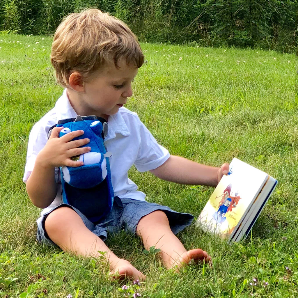 Child sitting on grass reading a book with a blue toy