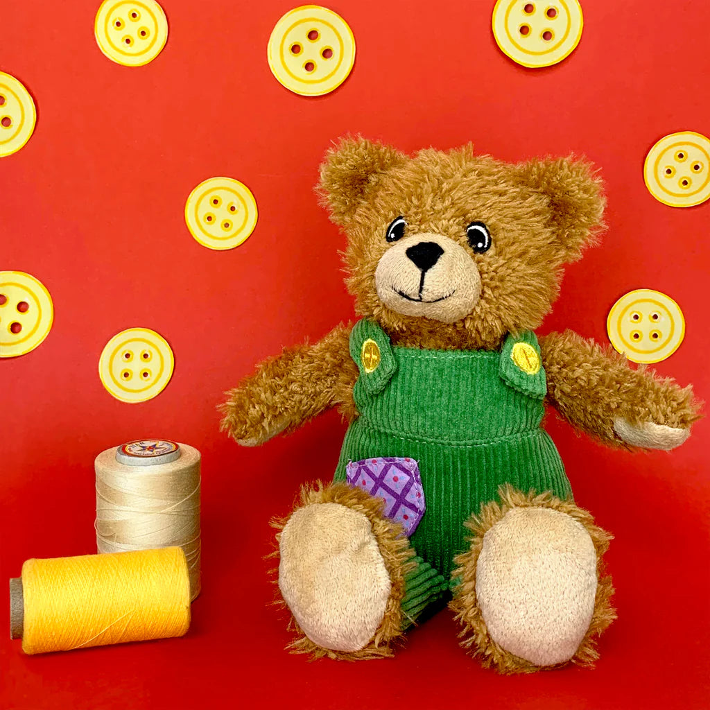 Teddy bear in a green outfit with buttons on a red background with button patterns