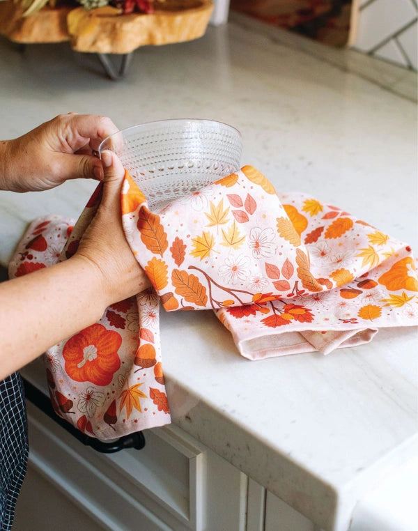 Person holding a stack of colorful kitchen towels with leaf patterns on a kitchen counter.