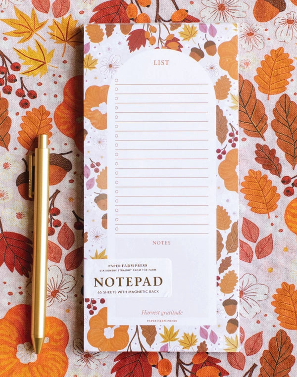 Notepad with a gold pen on a background with autumn leaf pattern