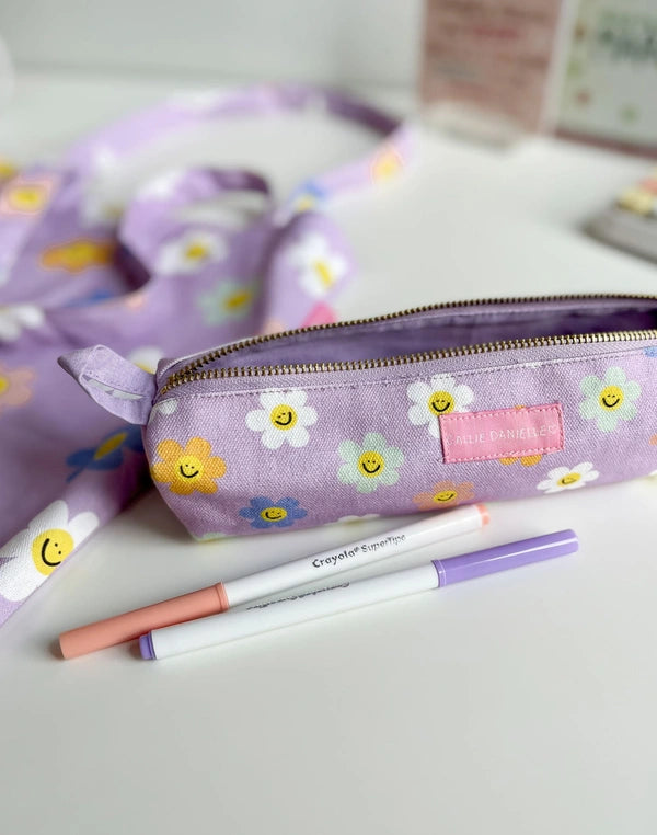 Purple pencil case with smiley face design on a white surface with markers.