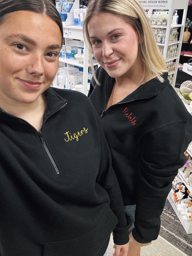 Two women wearing black jackets with embroidered text in a store setting.