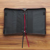 Black leather-bound book with red and black strings on a wooden surface