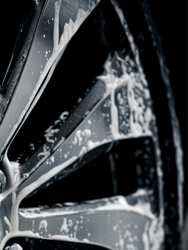 Close-up of a car's windshield wiper blade with water droplets and soap suds on a dark background