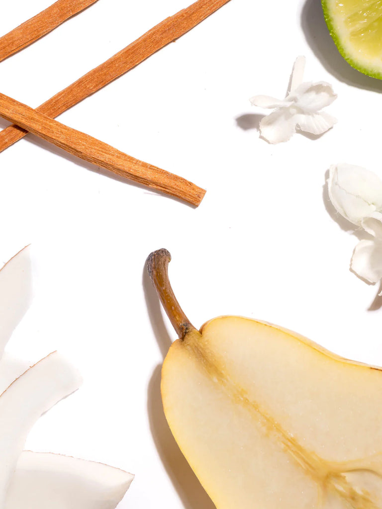 close up of driftwood, lime, flowers, and pear on a white background