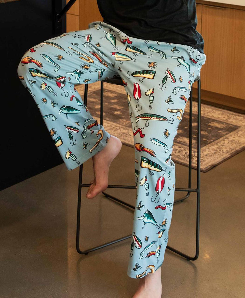 Person wearing pajama pants with fishing lure pattern sitting on a chair.