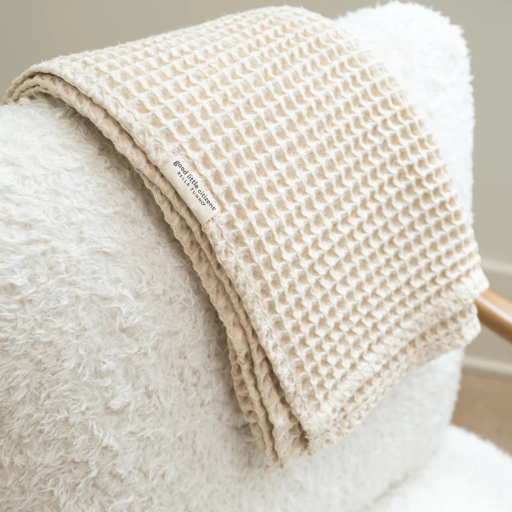 Beige textured blanket draped over a white armchair with a visible brand label.