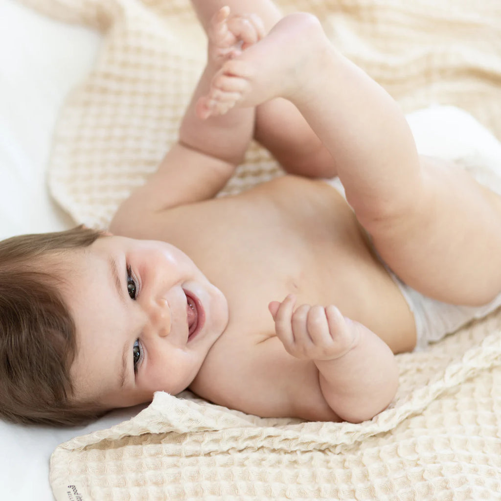 Baby lying on a beige blanket with a happy expression