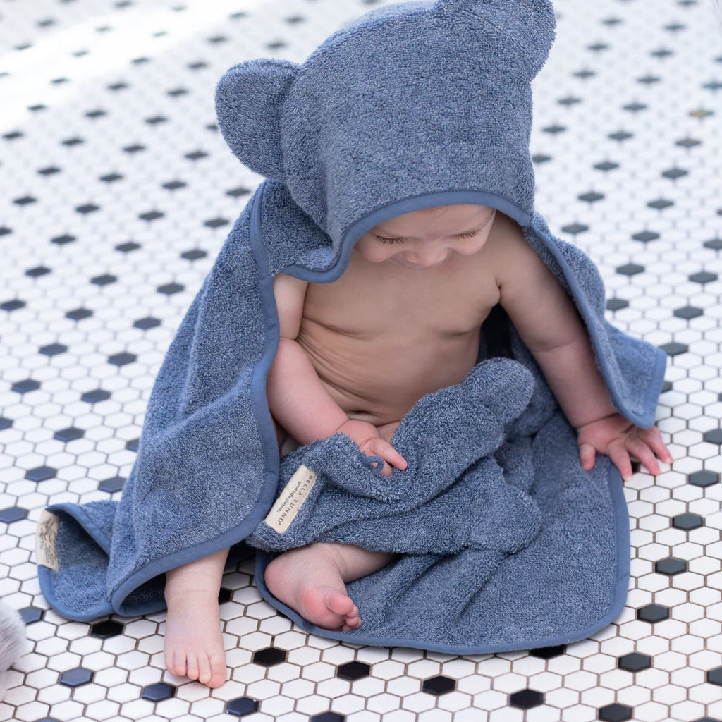 Baby wrapped in a blue hooded towel on a tiled floor