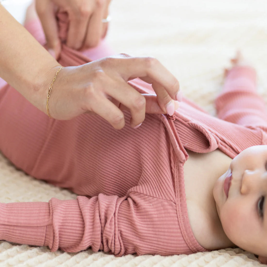 Baby in pink outfit being helped by an adult on a light-colored surface