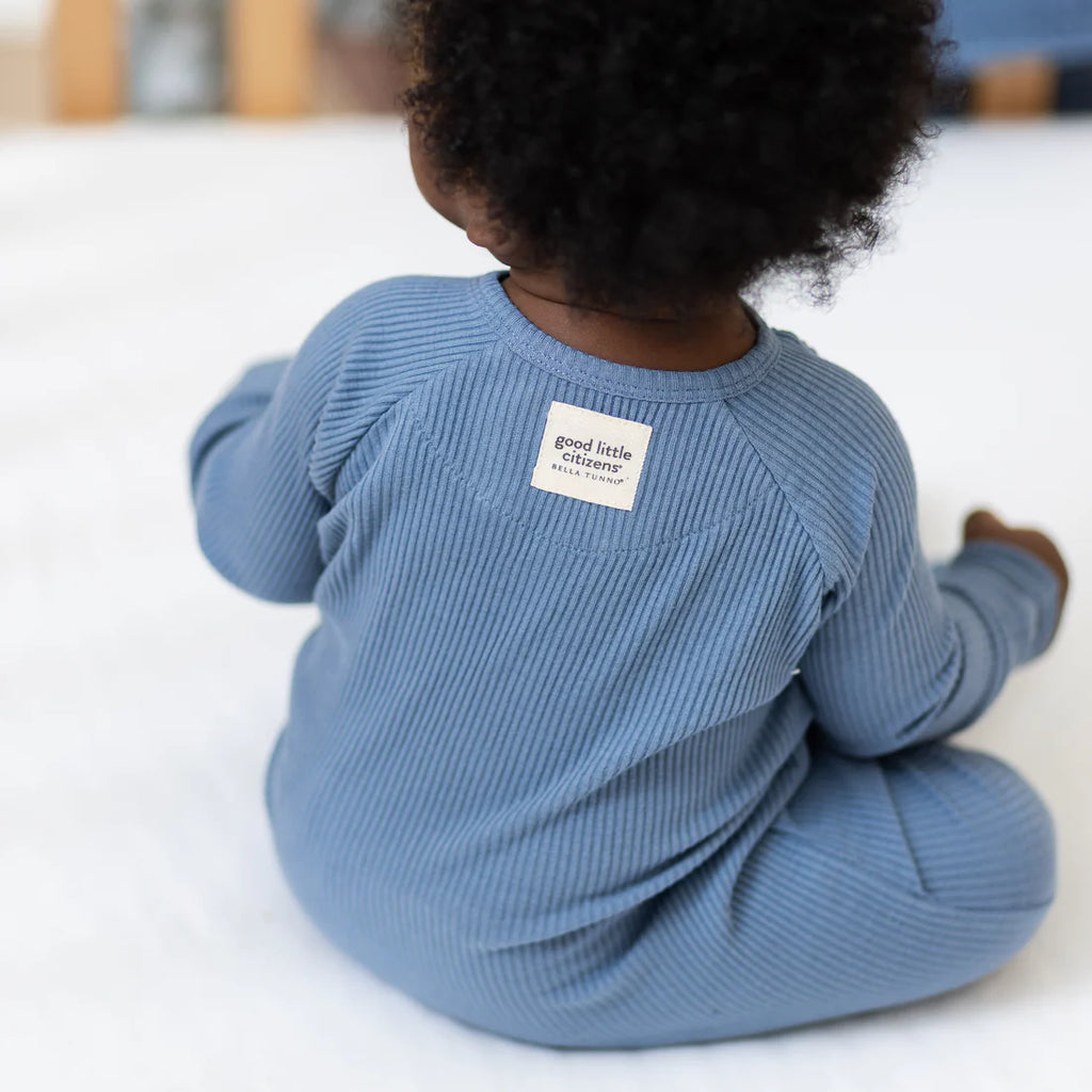 Baby wearing a blue ribbed outfit with a visible brand label on a light background