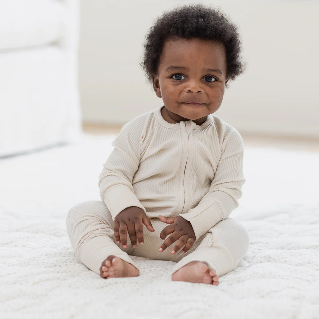 Baby wearing a white outfit sitting on a white surface