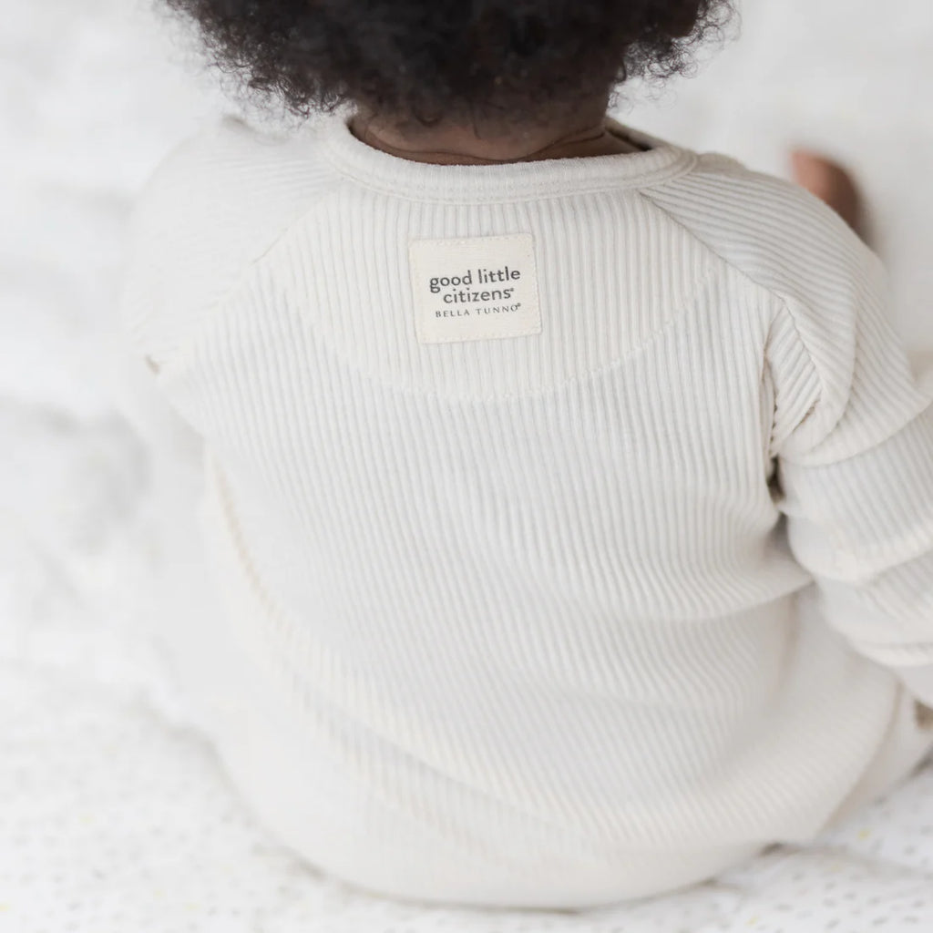 Baby wearing a white ribbed sweater with 'good little citizens' label on a light background