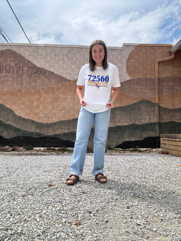 Person wearing a white t-shirt with text standing on a gravel surface.