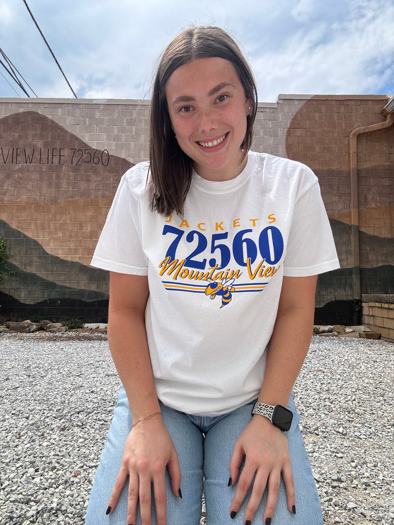 Person wearing a white t-shirt with text and numbers, standing outdoors.