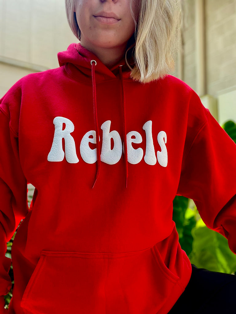 Person wearing a red hoodie with 'Rebels' printed on it, standing outdoors.