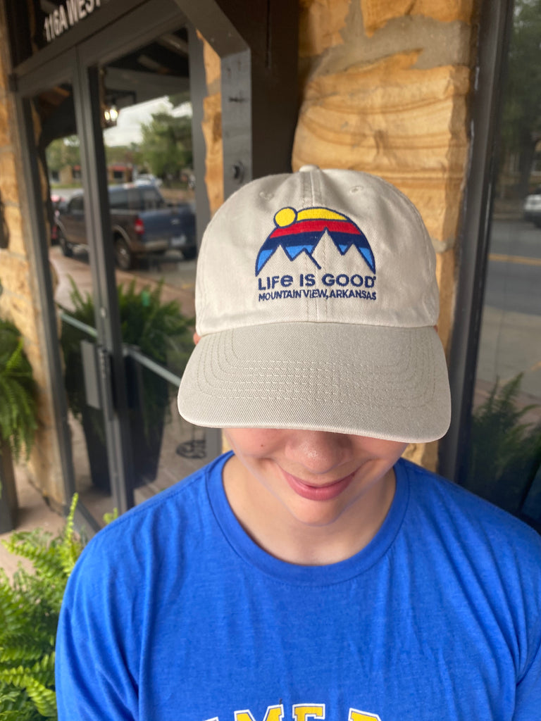 life is good hat being worn in front of rock building