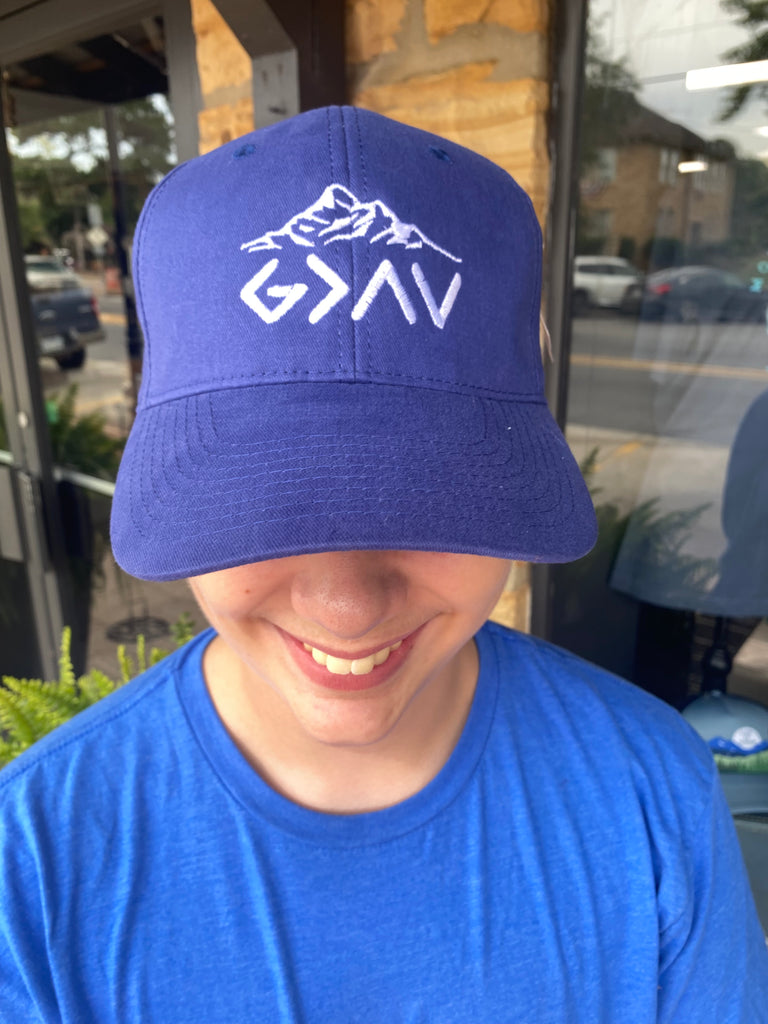 God is greater than highs and lows cap being worn outside in front of a rock building