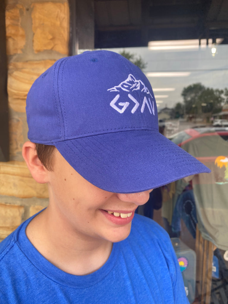 God is greater than highs and lows cap being worn outside in front of a rock building