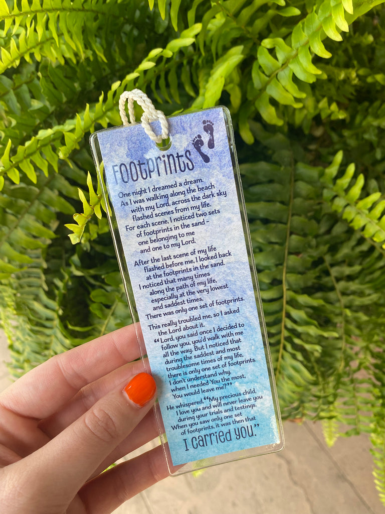 footprints bookmark in a clear plastic cover in front of a green fern