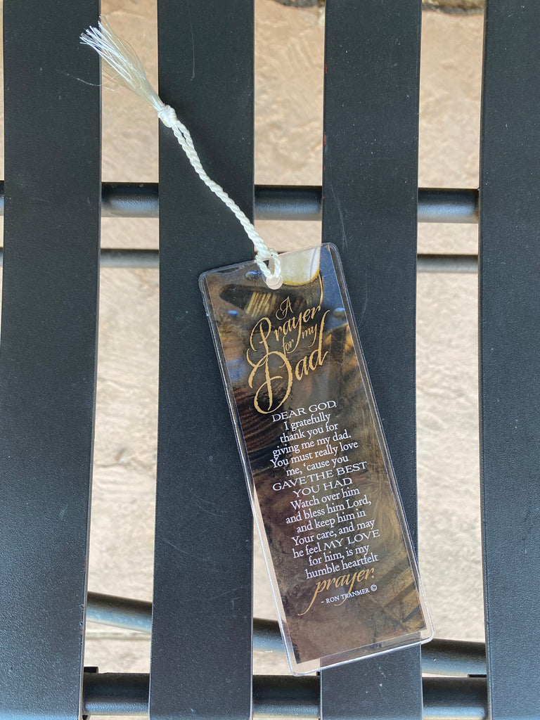 A prayer for my dad bookmark in a clear plastic covering with a white braided on a black metal bench
