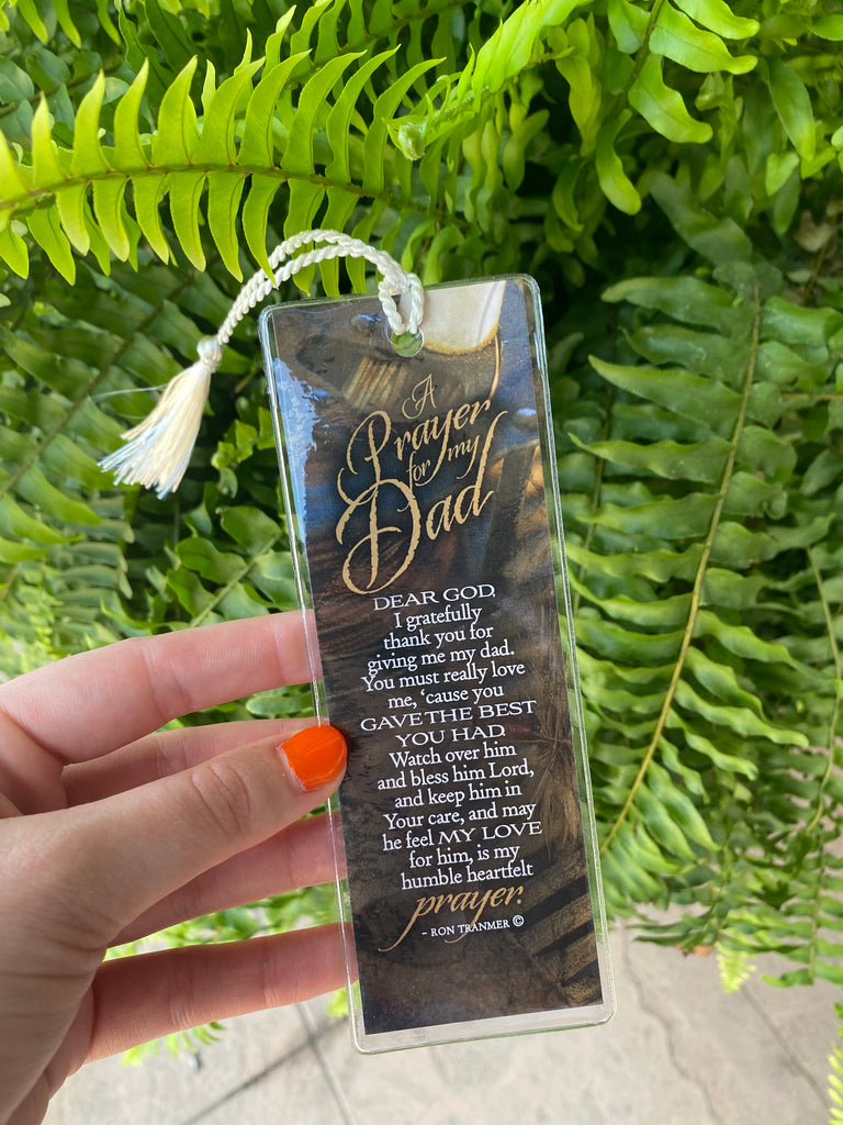 A prayer for my dad bookmark with a clear plastic covering and a white braided rope being held up in front of a fern bush