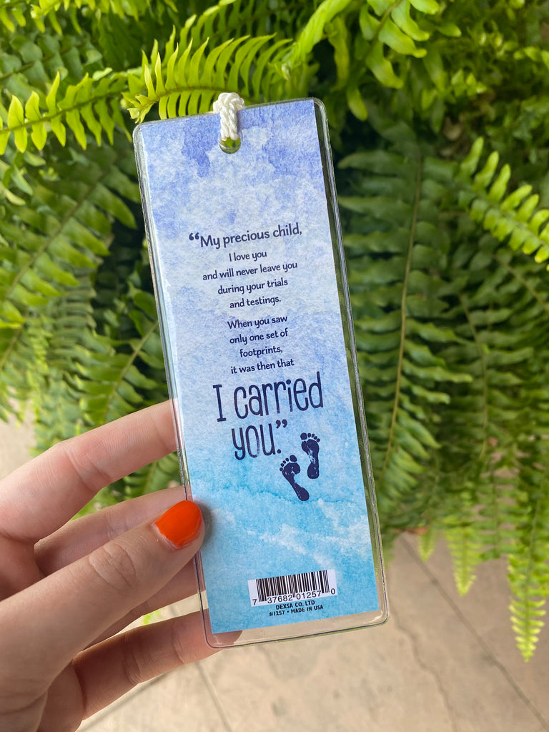 footprints bookmark in a clear plastic cover in front of a green fern