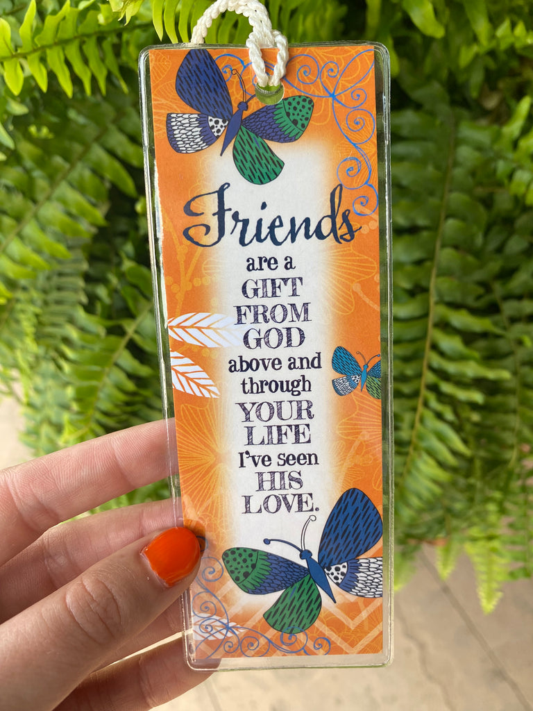 friends are a gift bookmark in a clear plastic cover being held in front of a green fern