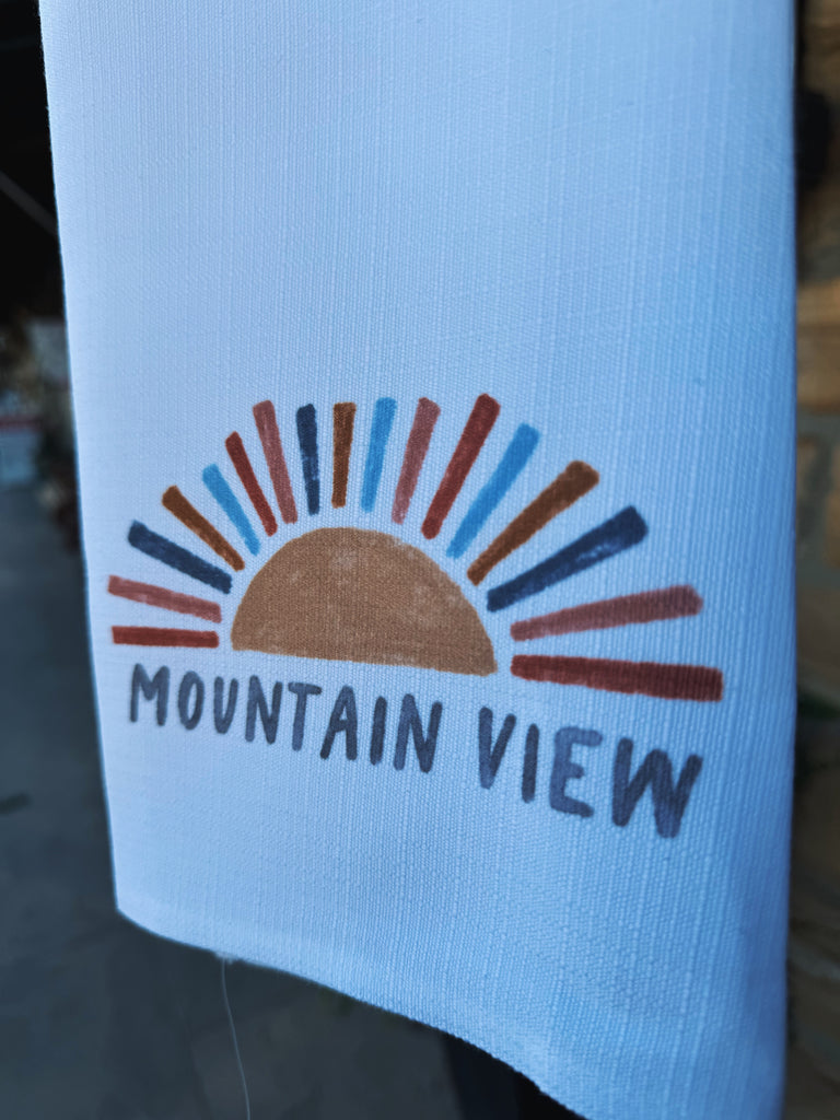 sunshine mountain view tea towel being held in front of a rock building