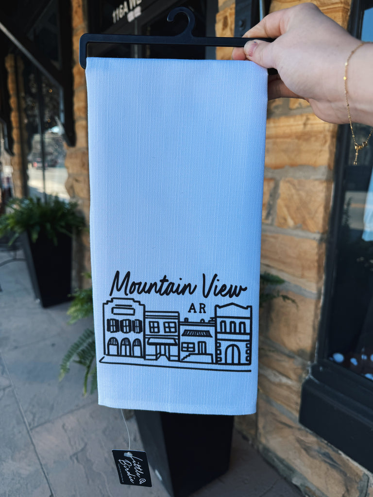 mountain view mainstreet tea towel being held in front of a rock wall