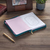 Open notebook with pink interior on a wooden surface, next to a pen and photo frame.