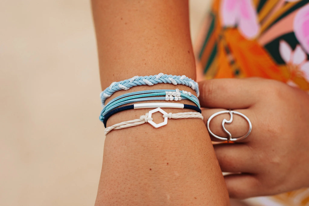 Close-up of a wrist with multiple bracelets and two rings on a neutral background