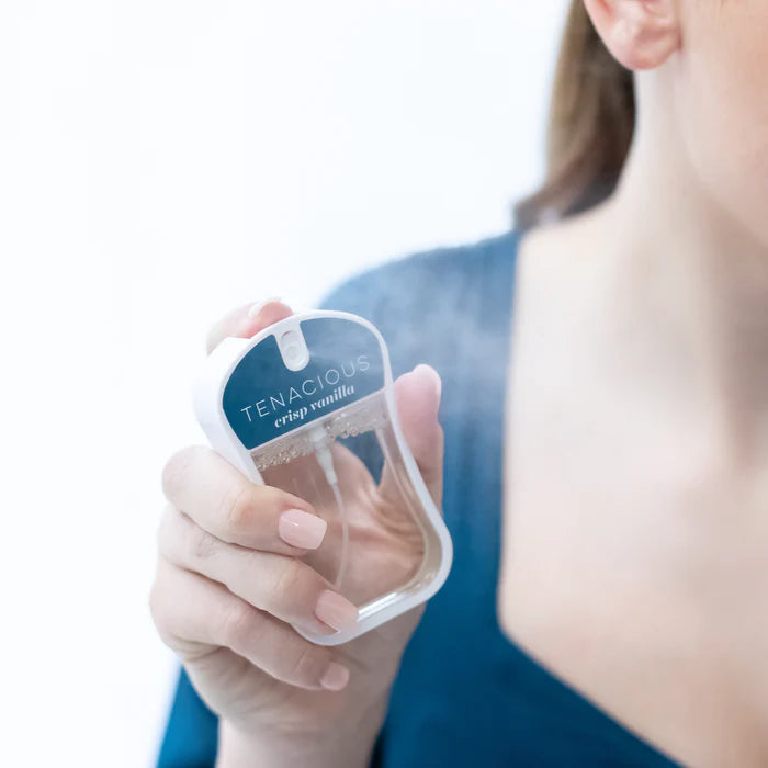 Hand holding a small container labeled 'Tenacious' against a blurred background