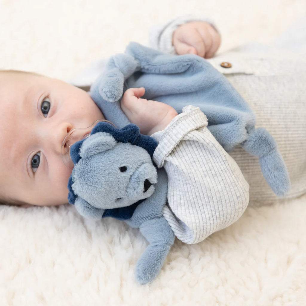 Baby holding a blue plush toy with a lion design on a white blanket