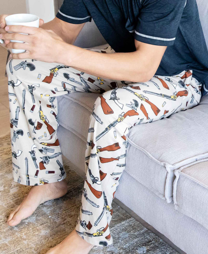 Person wearing pajama pants with gun print sitting on a couch holding a mug.
