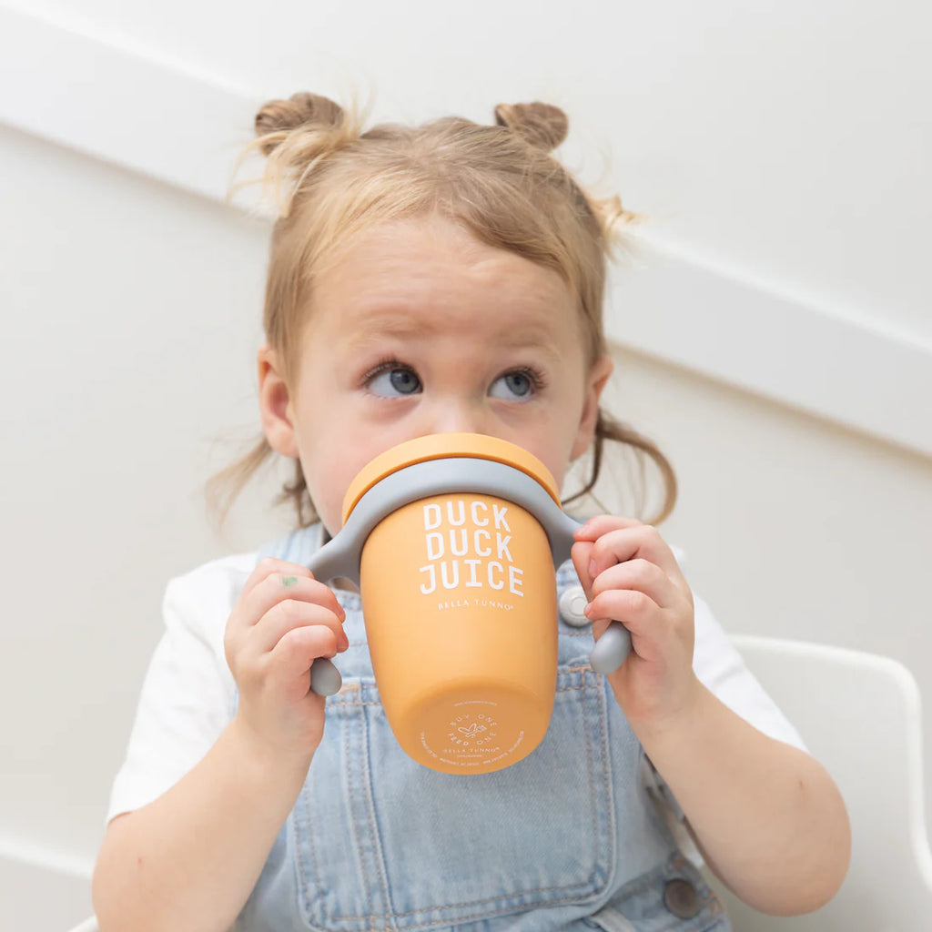 Child holding a yellow cup with 'Duck Duck Juice' text against a white background