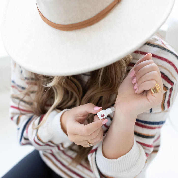 Person applying sunscreen to their arm with a hat on, wearing a striped sweater.