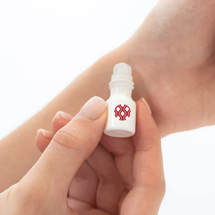 Small white bottle with a red logo held between fingers against a light background