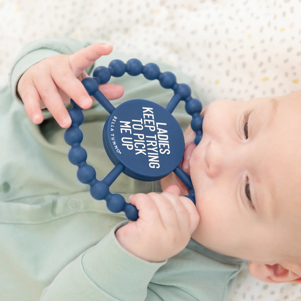 Baby holding a blue teething ring with text