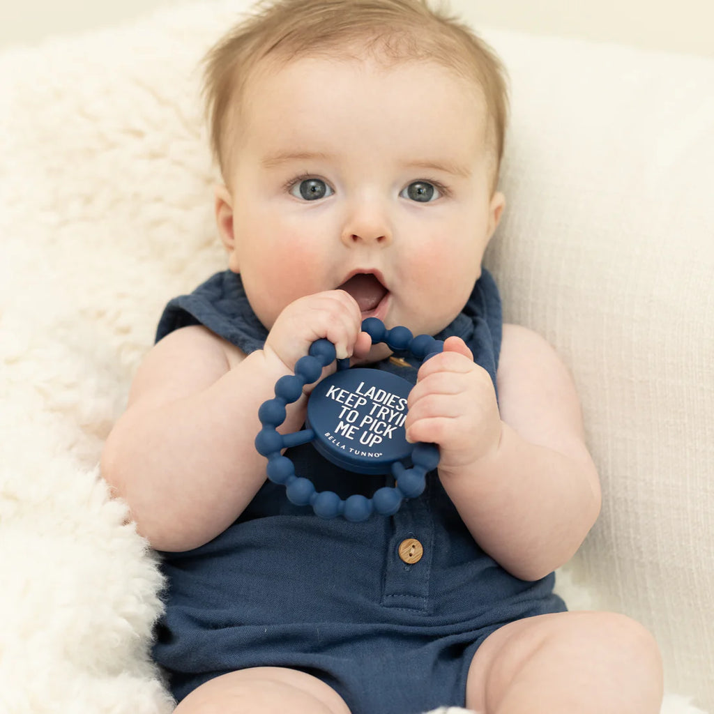 Baby holding a blue teething ring with text on a white blanket