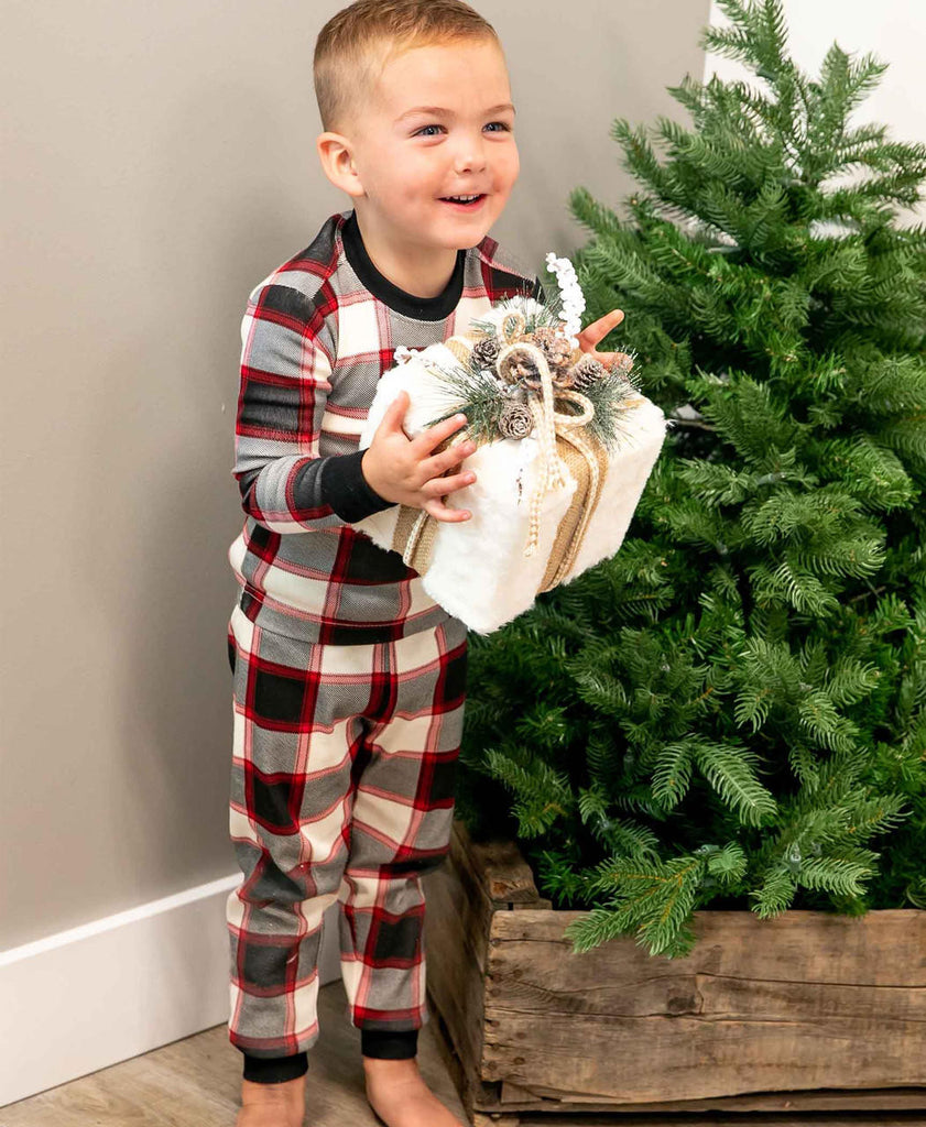 Child in plaid pajamas holding a gift basket next to a Christmas tree.