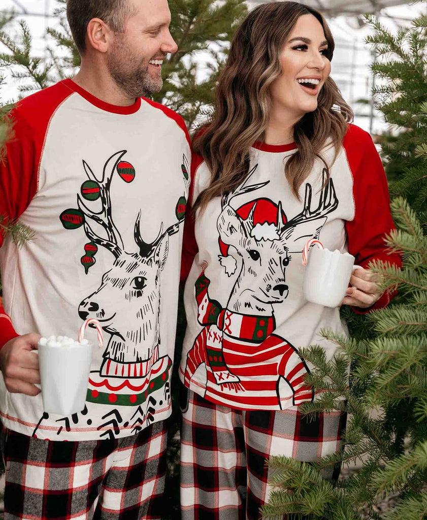Two people wearing matching Christmas-themed pajamas with reindeer designs, standing in front of a decorated Christmas tree.