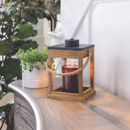 Wooden lantern with a candle on a wooden surface next to a plant