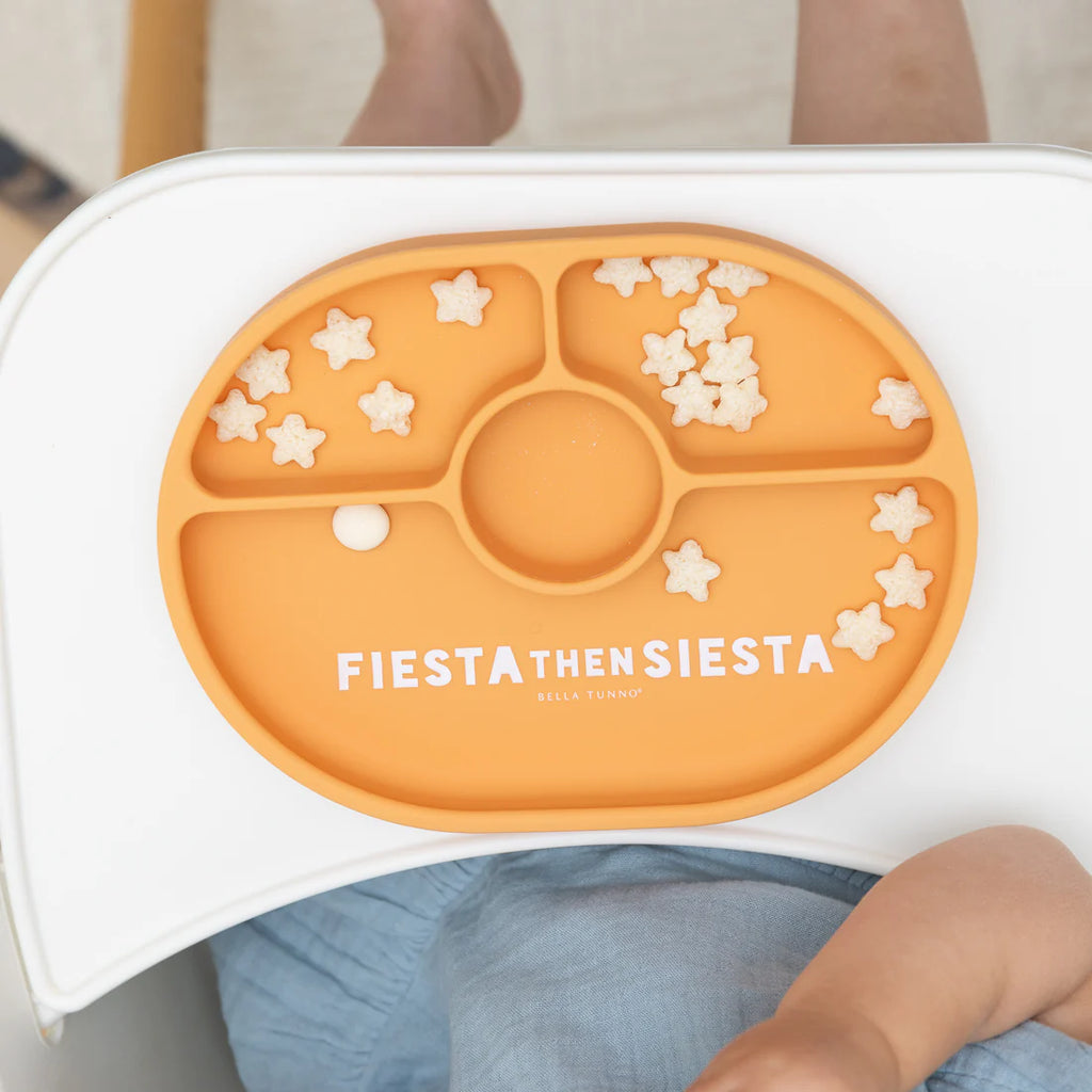 Orange children's plate with star patterns and 'FIESTA THEN SIESTA' text, held by a child.