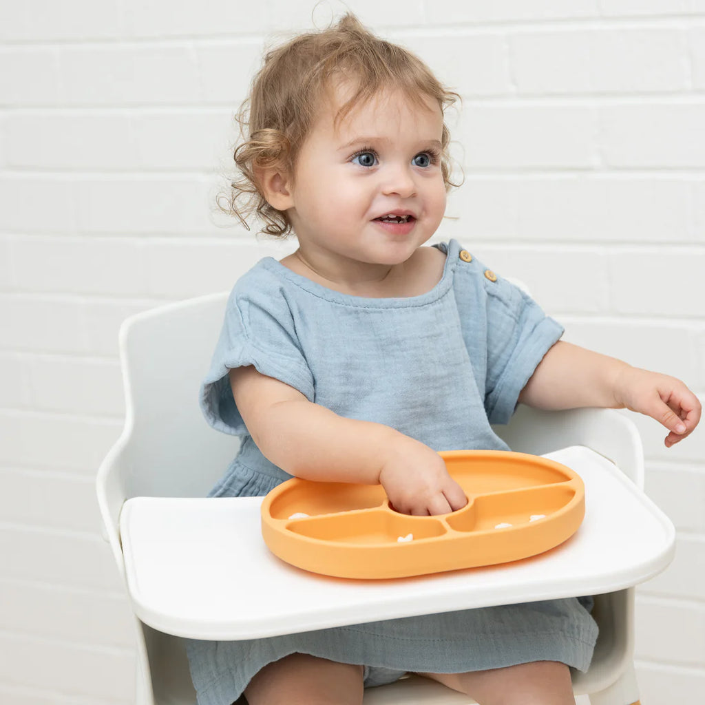 Child sitting in a high chair with an orange plate on a white background
