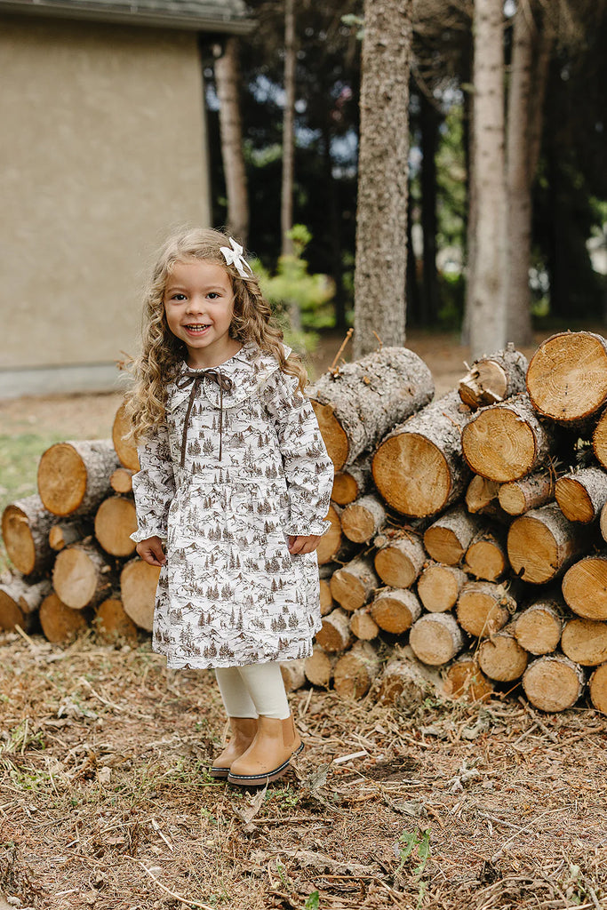 Young girl standing in front of a stack of logs with a blurred background