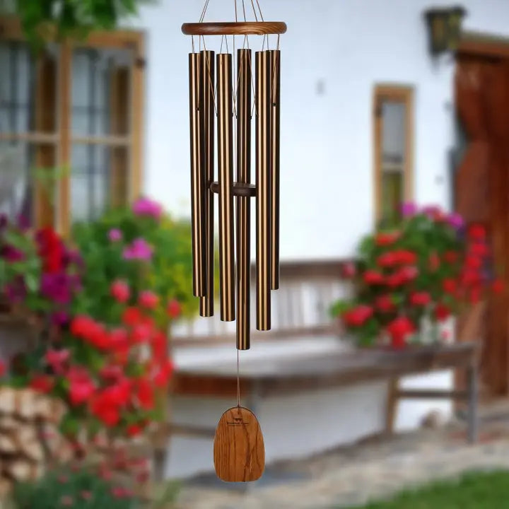 wind chime in front of a building with various shades on pink and red flowers blurred in the background